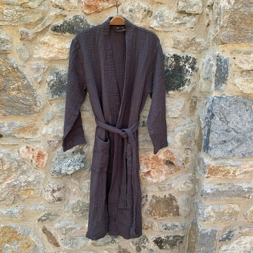 front view of charcoal muslin robe hanging in front of a stone wall.