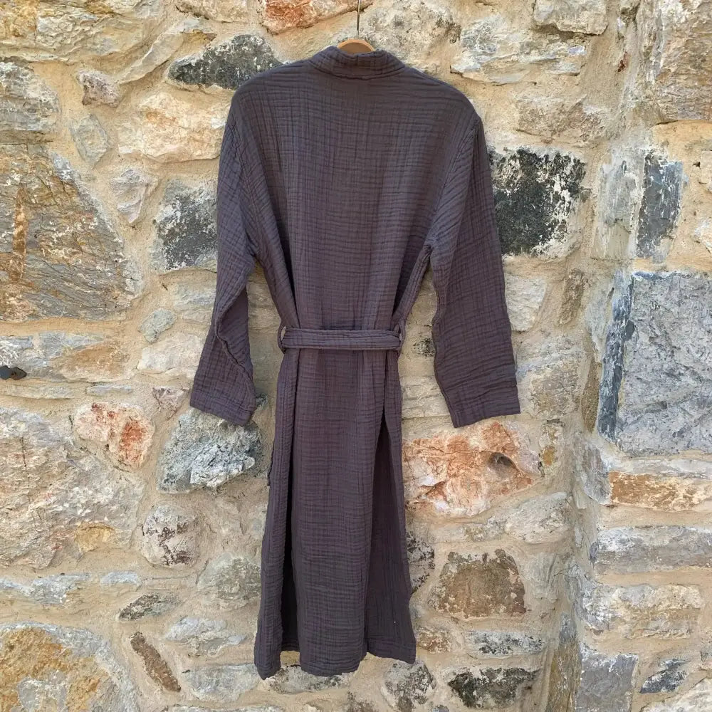 Back view of charcoal muslin robe hanging in front of a stone wall.