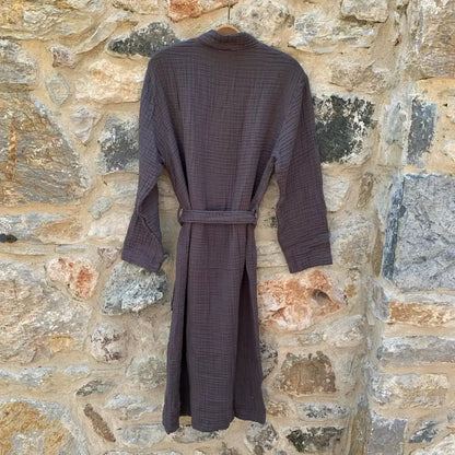 Back view of charcoal muslin robe hanging in front of a stone wall.