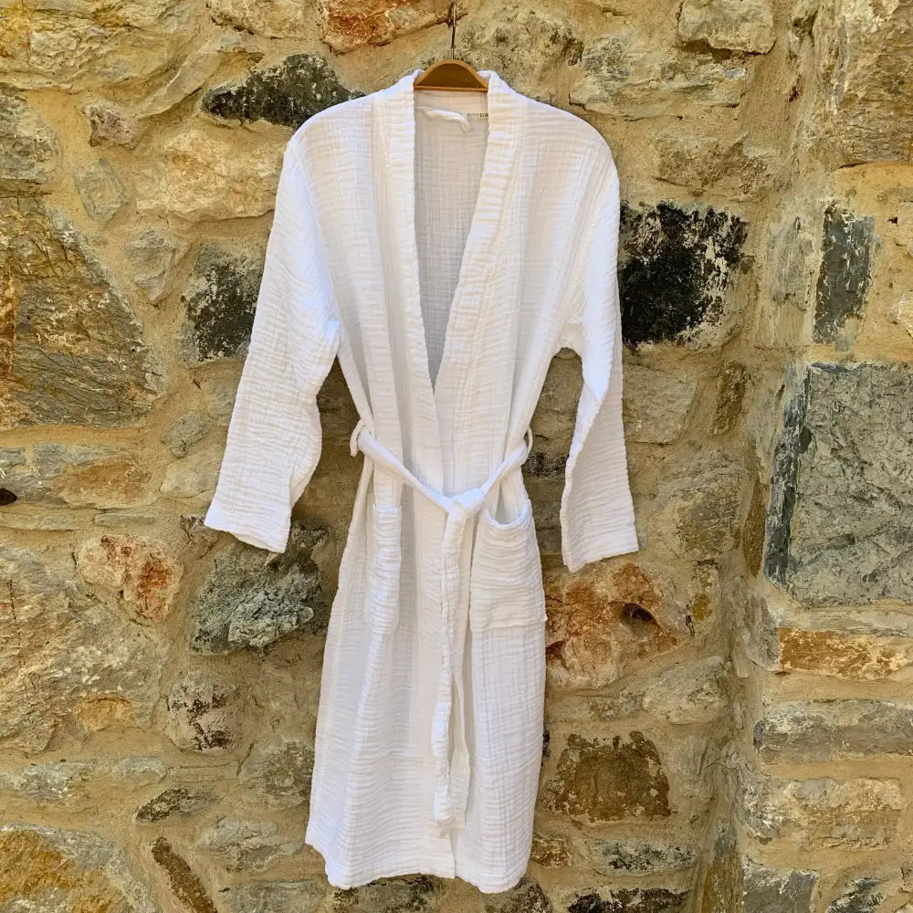 A white muslin bathrobe hanging in front of a stone wall.
