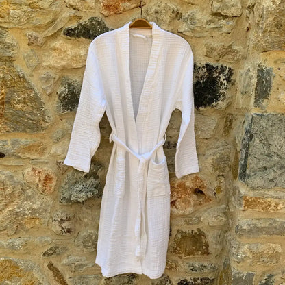 A white muslin bathrobe hanging in front of a stone wall.