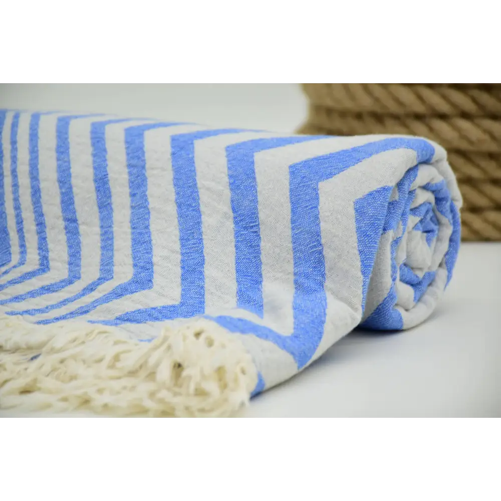 A rolled turkish towel with zigzag design pale sax blue stripes and cream-colored fringe in soft cotton material