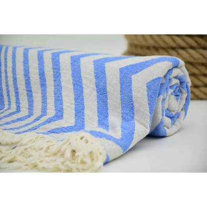 A rolled turkish towel with zigzag design pale sax blue stripes and cream-colored fringe in soft cotton material