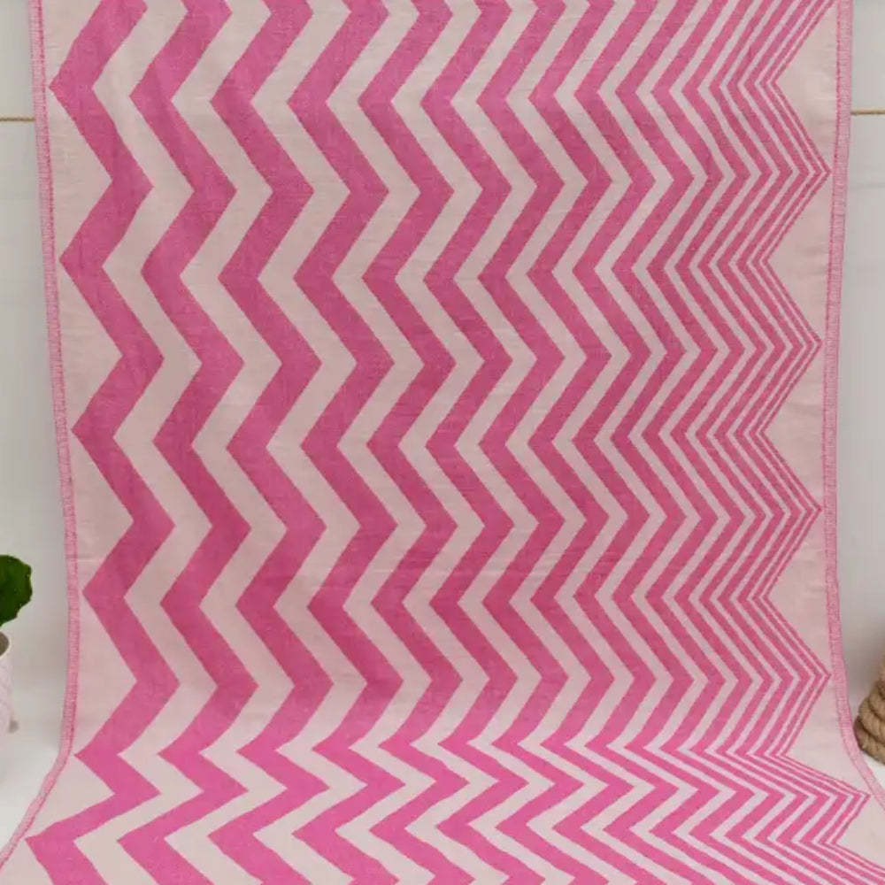 A vibrant pink and white zigzag pattern peshtemal towel with a soft textured weave perfect for beach or bath use