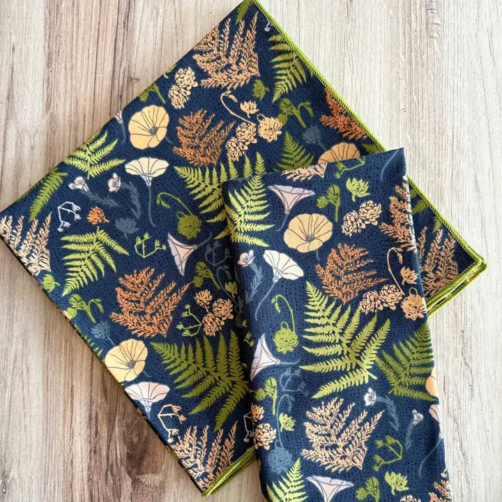 Two blue patterned towels with nature-themed designs on a wooden surface