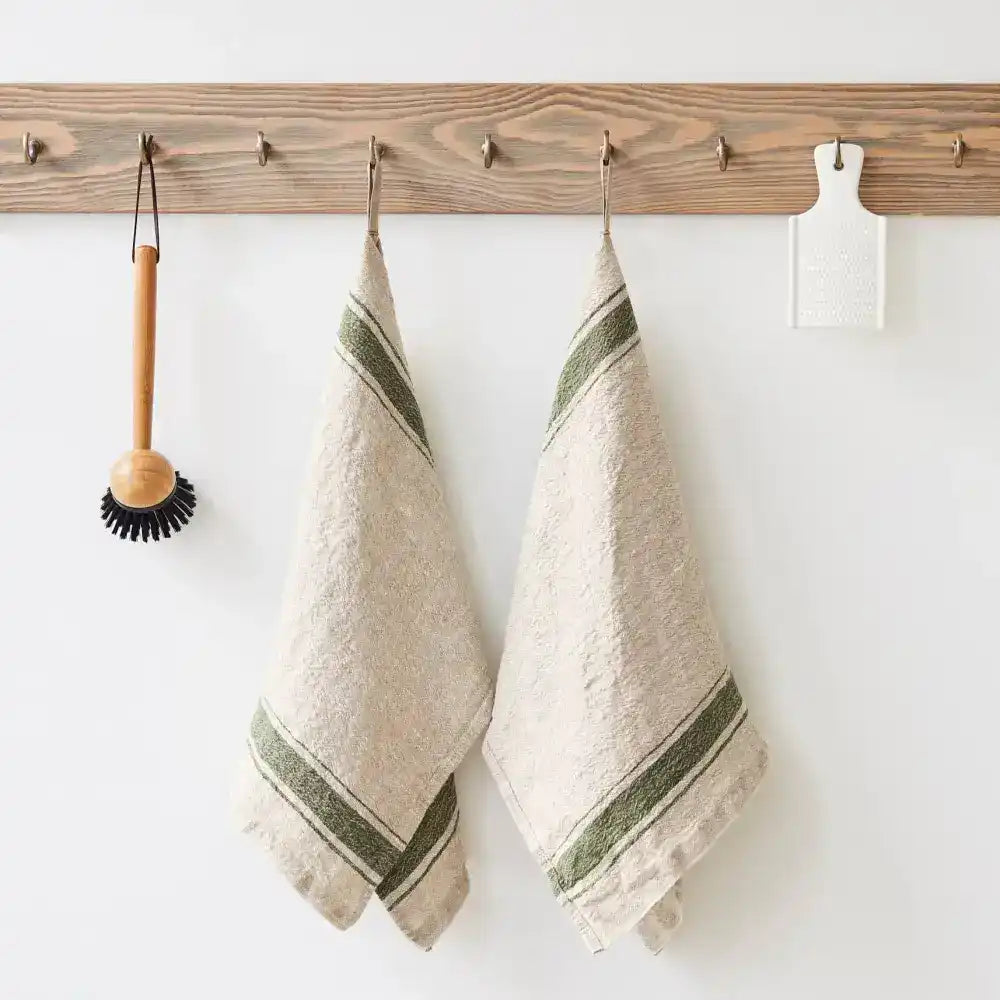 A natural color kitchen towel with green stripes hanging on a hook next to kitchen utensils.