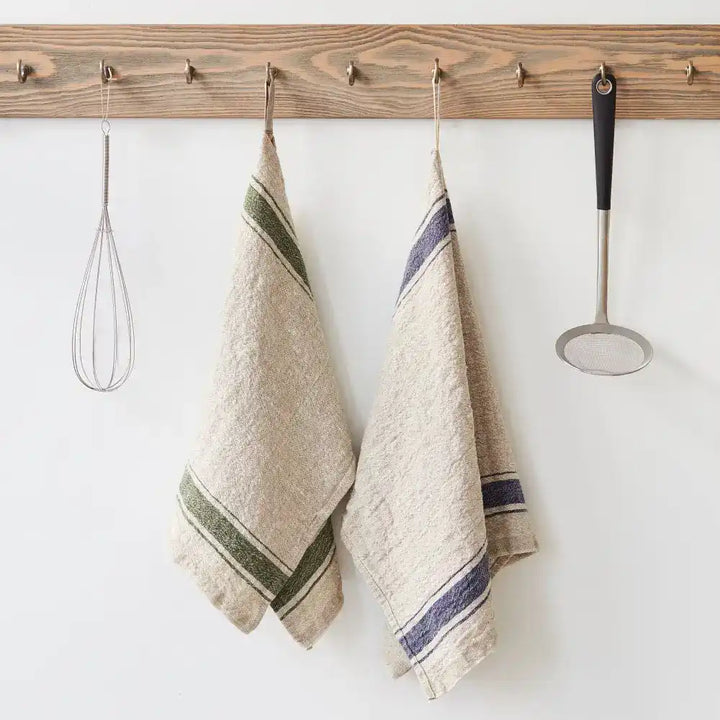 A natural color kitchen towel with green and blue stripes hanging on a hook next to kitchen utensils.