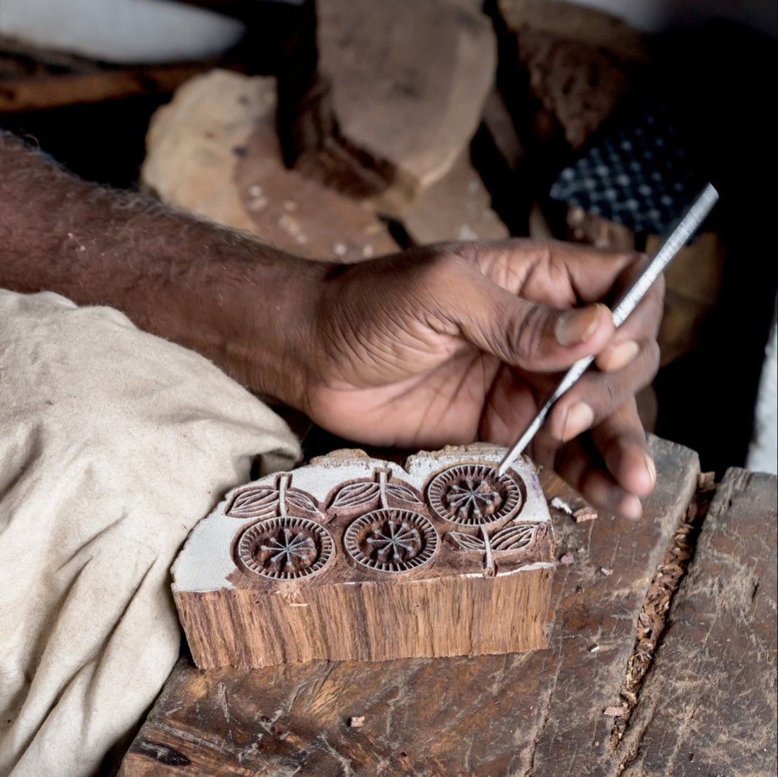 Person working with a wooden stamp block and metal tool on a rustic surface.