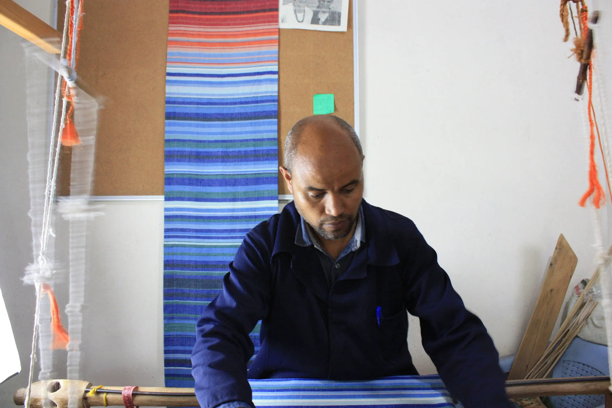A man in a dark blue jacket weaving a handmade climate warming ethiopian handwoven table runner with bright stripes