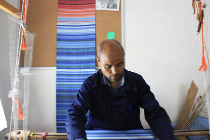 A man in a dark blue jacket weaving a handmade climate warming ethiopian handwoven table runner with bright stripes