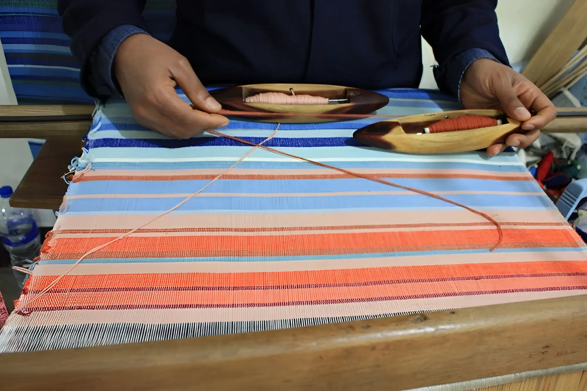 A handmade climate warming table runner with vibrant blue orange and pink stripes woven on a wooden loom