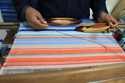 A handmade climate warming table runner with vibrant blue orange and pink stripes woven on a wooden loom