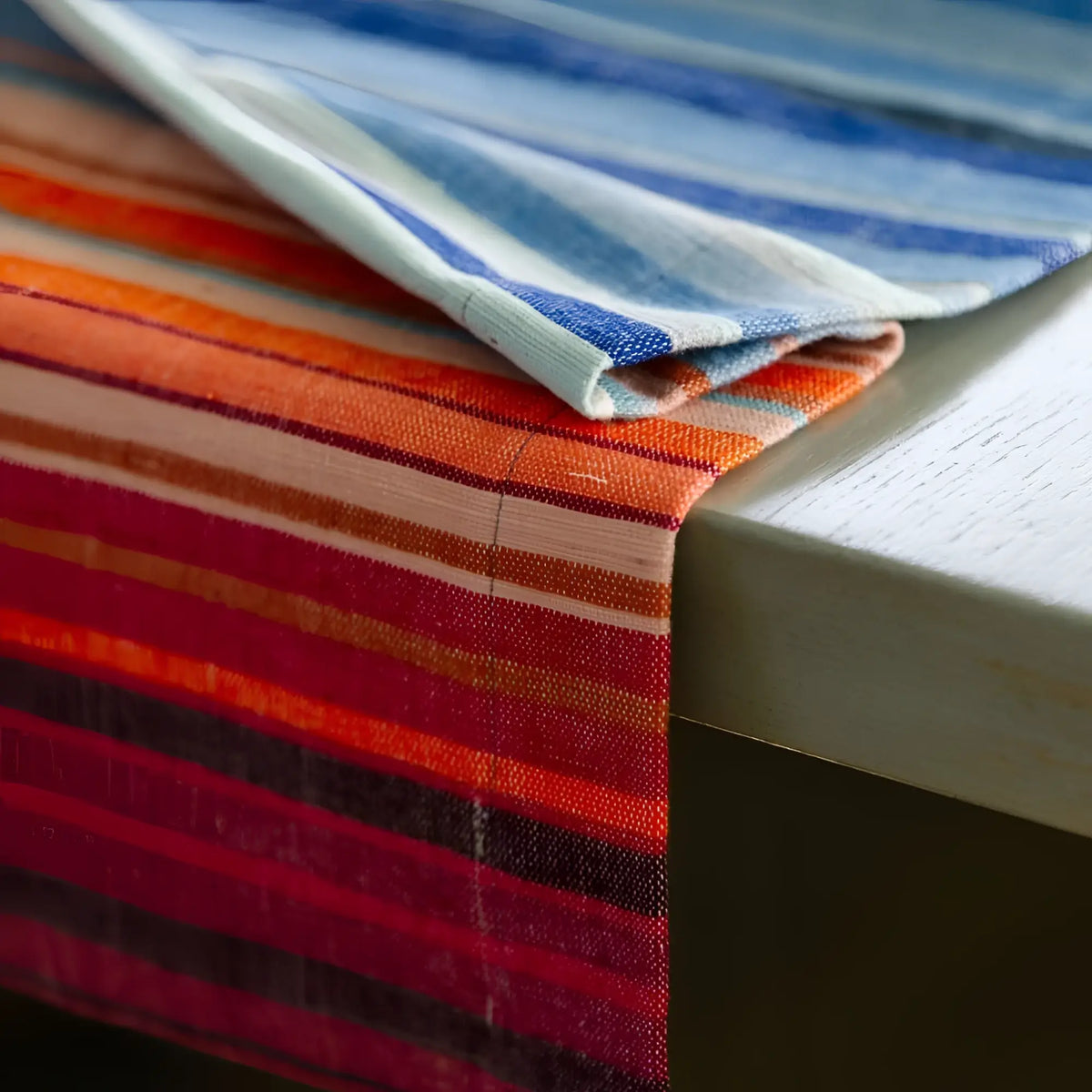 A handmade climate warming table runner in vibrant striped linen with reds, oranges, blues, and whites