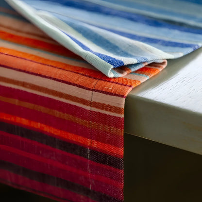 A handmade climate warming table runner in vibrant striped linen with reds, oranges, blues, and whites