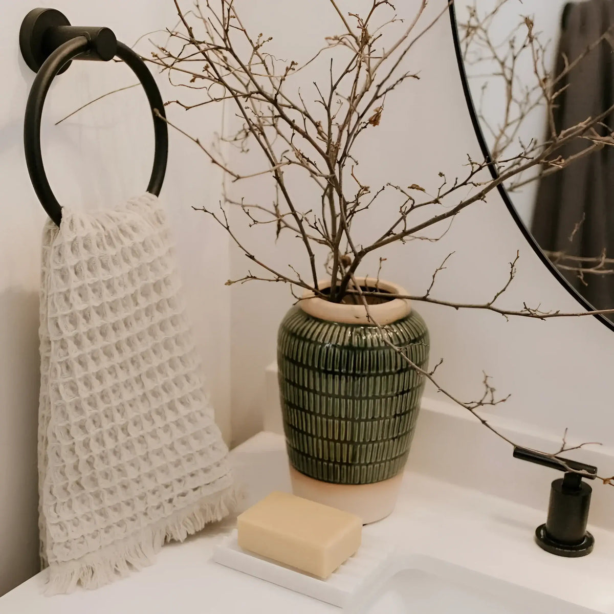 Green ceramic vase with textured stripes holding natural branches, perfect for your waffle bath towel setup