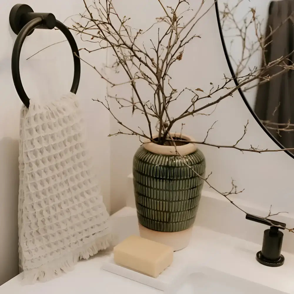 Green ribbed ceramic vase with beige rim holding dried branches next to waffle soft turkish cotton hand towel made of pure aegean cotton