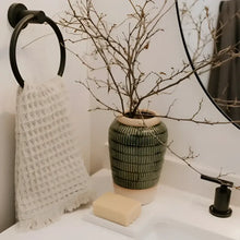 Green ribbed ceramic vase with beige rim holding dried branches next to waffle soft turkish cotton hand towel made of pure aegean cotton