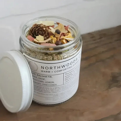 A clear glass jar with a white lid labeled northwoods co warm and comforting simmer pot blend for cozy cabin vibes