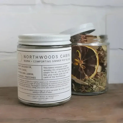 A clear glass jar with white lid filled with dried botanicals for warm and comforting northwoods cabin simmer pot blend