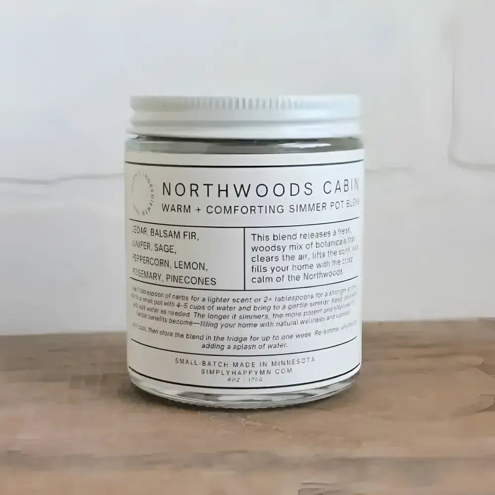 A clear glass jar with white lid containing a warm and comforting northwoods cabin simmer pot blend by simply happy