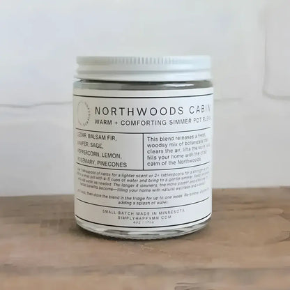 A clear glass jar with white lid containing a warm and comforting northwoods cabin simmer pot blend by simply happy