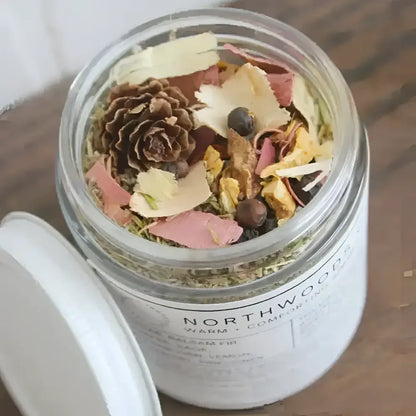 A clear glass jar with a white lid labeled northwood warm and comforting containing a colorful simmer pot blend