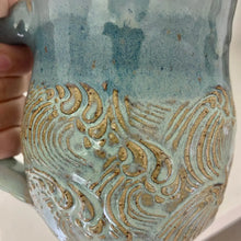 This handmade pottery mug features a textured sea-foam wave design with ocean blue rim.