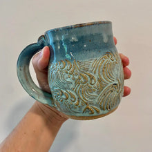 This handmade pottery mug features a textured sea-foam wave design with ocean blue rim.