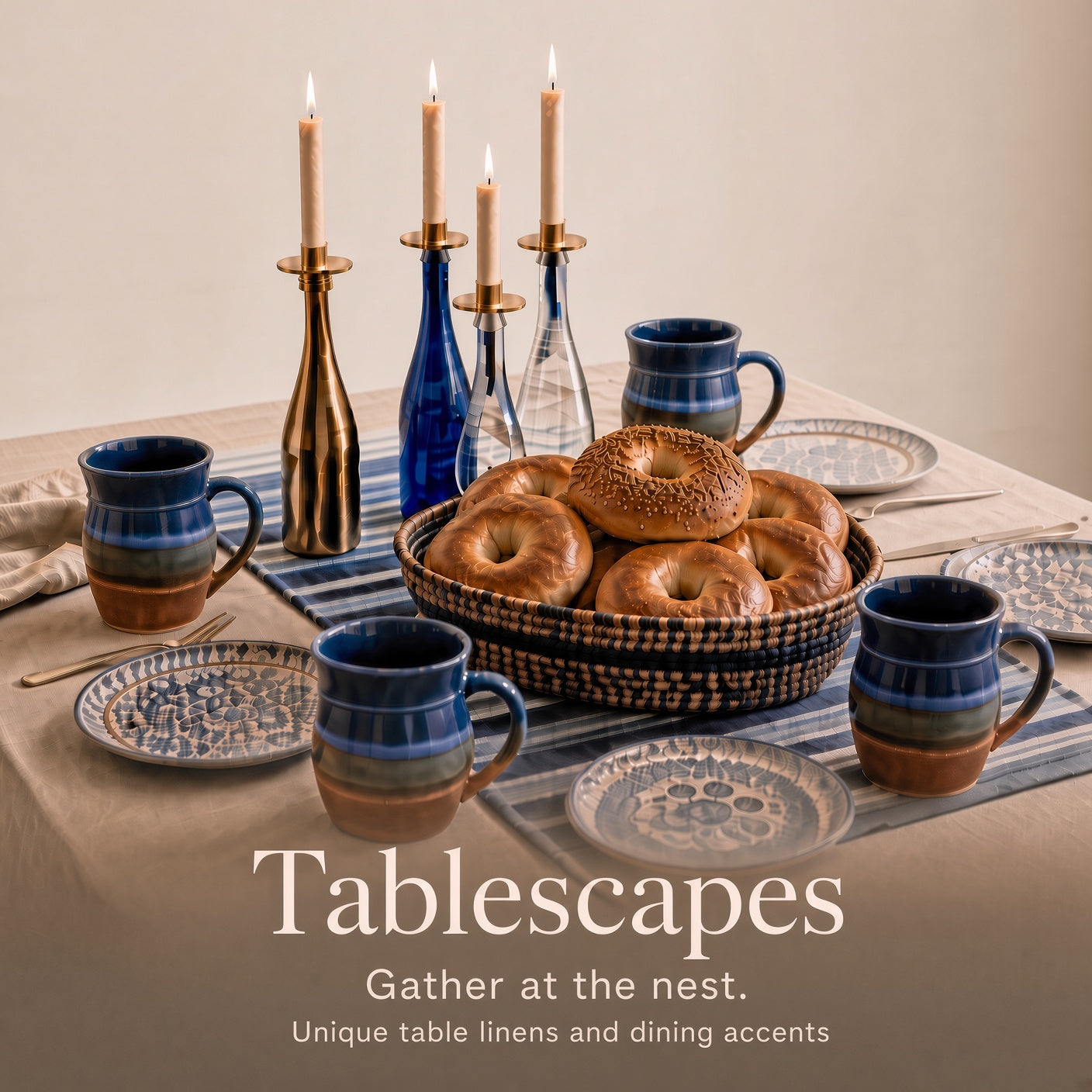 A styled dining table setting with ceramic mugs, plates, and table linens in blue, navy, and brown tones, with a basket of bagels in the center and lit candles in the background. Text at the bottom reads 'Tablescapes Gather at the nest.