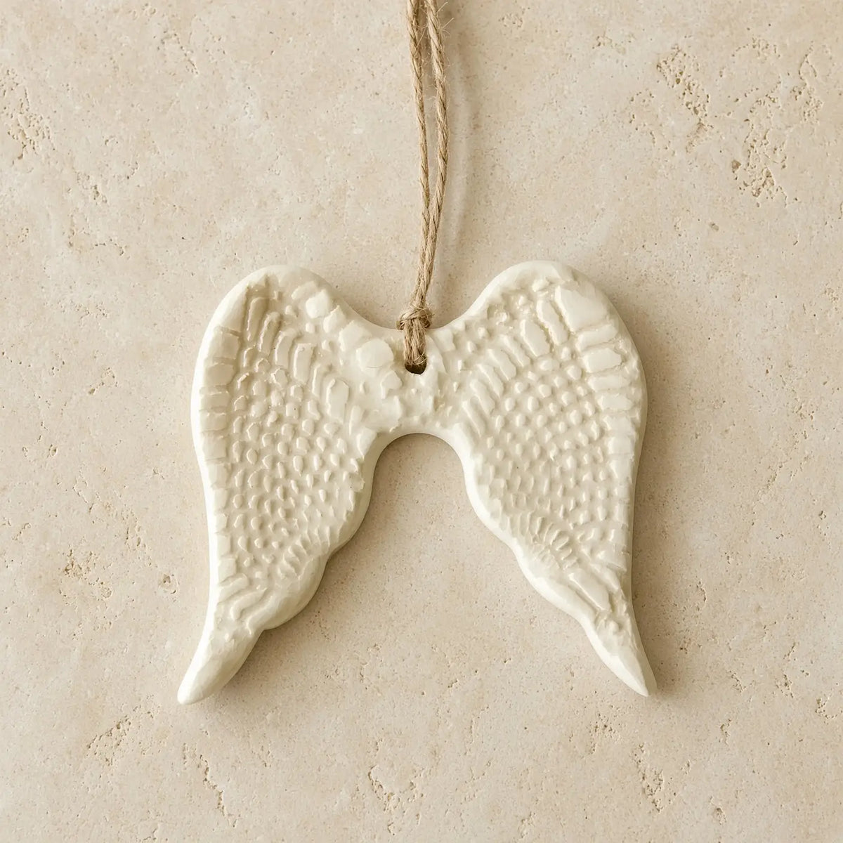 White ceramic angel wing ornament with textured feather patterns and natural twine hanger for year-round gifting