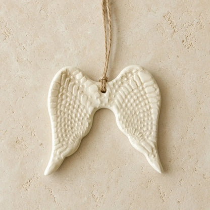 White ceramic angel wing ornament with textured feather patterns and natural twine hanger for year-round gifting
