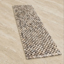 A woven bath mat made of natural stone tiles in beige and gray paired with a whitewash rosewood table runner