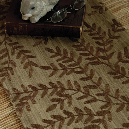 Beige table runner with chocolate brown woven leaf design.