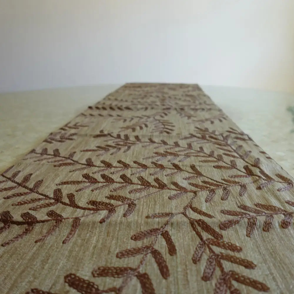 Beige table runner with chocolate brown woven leaf design.