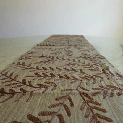 Beige table runner with chocolate brown woven leaf design.