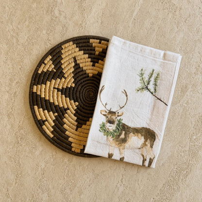 White linen winter tea towel with watercolor deer and pine branch paired with african zulu trivet nest