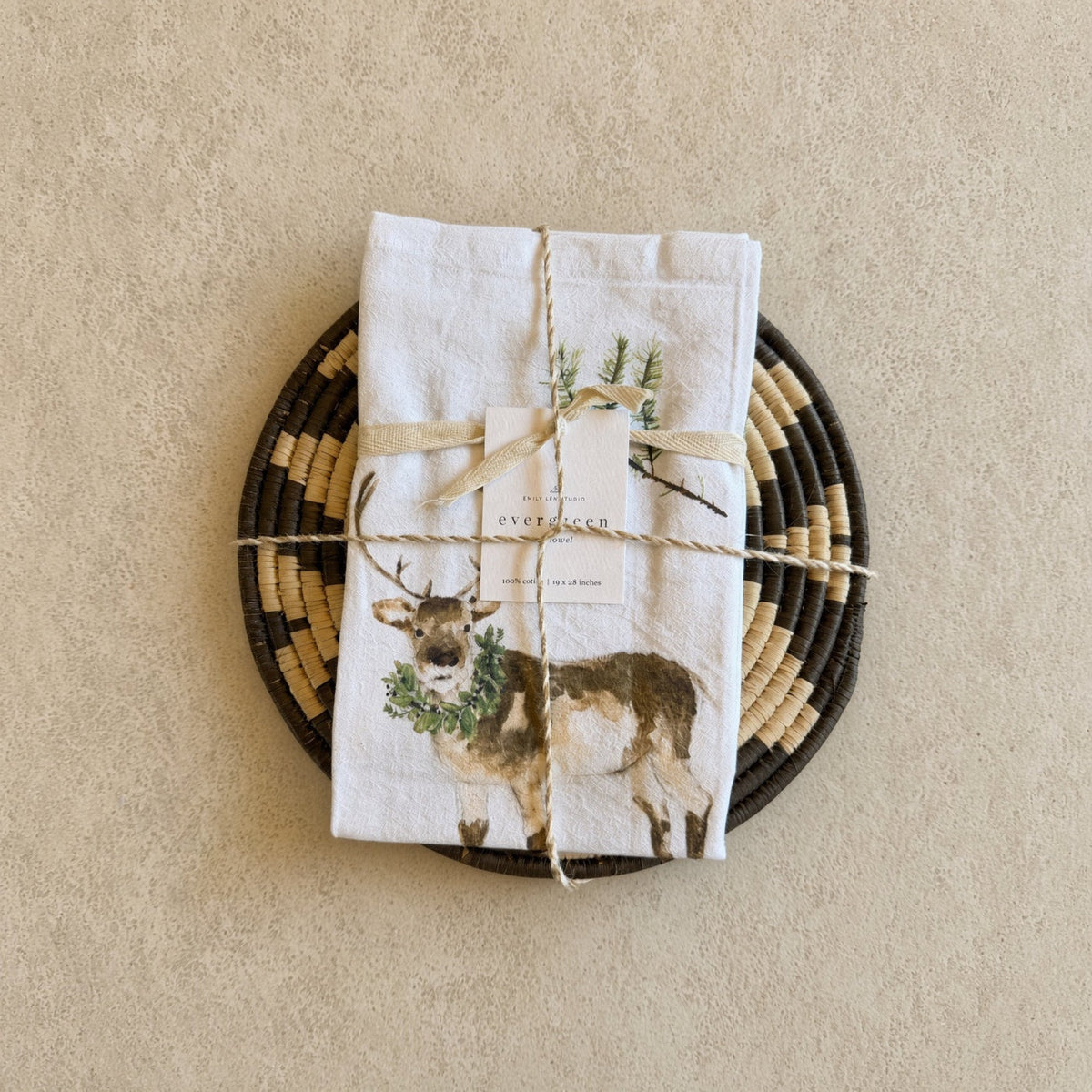 White linen tea towel with brown deer and greenery tied with twine paired with african zulu trivet nest