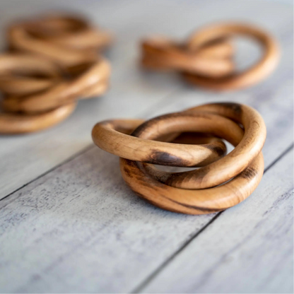 A close up of an interlocking wooden napkin ring with three others in a blurred background.