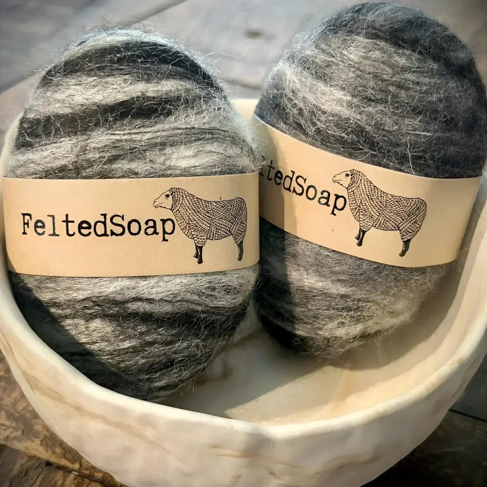 Two felted soap bars with 'FeltedSoap' labels in a stone bowl.