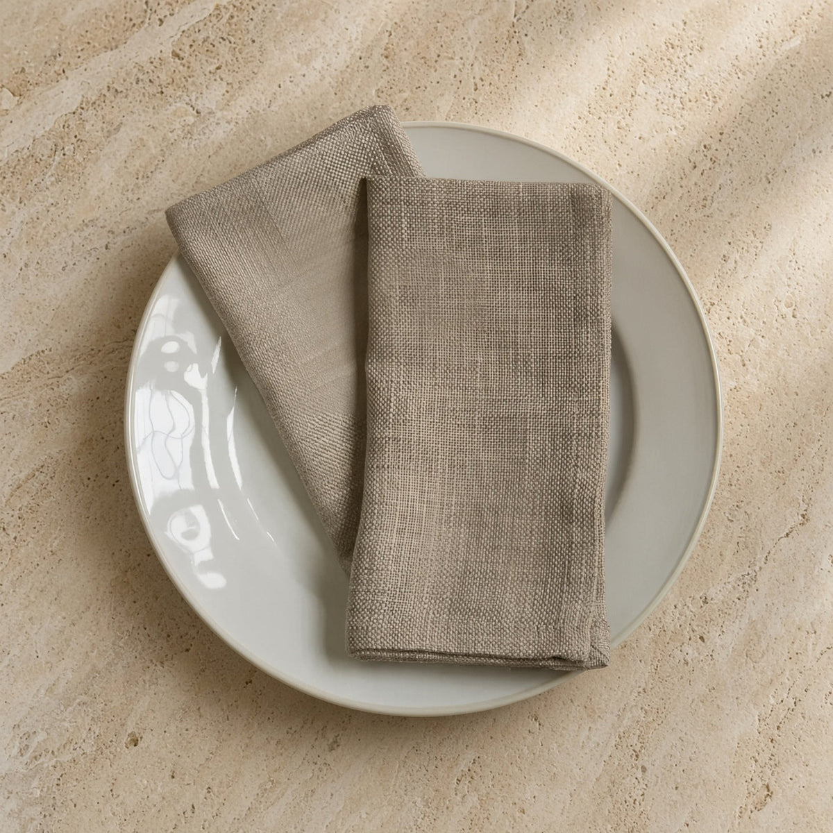 Beige linen cloth napkins in oyster color with subtle woven texture neatly folded on a white plate set of 4