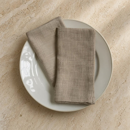 Beige linen cloth napkins in oyster color with subtle woven texture neatly folded on a white plate set of 4