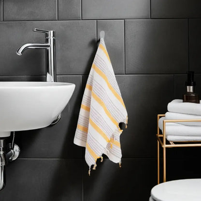 Ivory and yellow Turkish cotton hand towel with tassels hanging on a hook